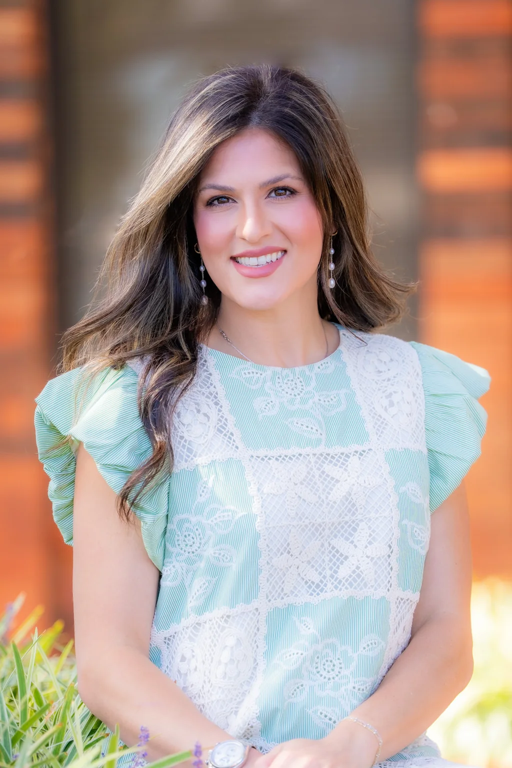 Julia Klug, PA-C, smiling, in a mint dress, seated by a planter outside the office